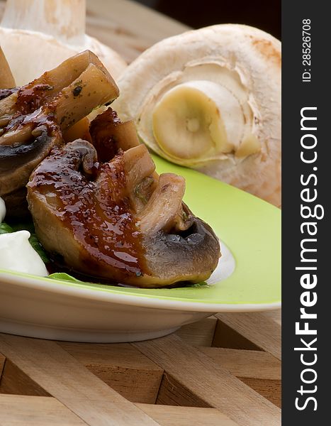 Cooked Grill Champignons with Sauce and Sour Cream Plate closeup on Wood Square background and Raw Mushrooms. Cooked Grill Champignons with Sauce and Sour Cream Plate closeup on Wood Square background and Raw Mushrooms