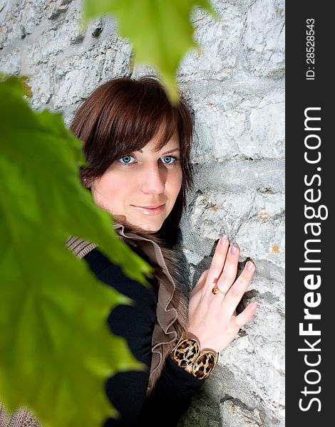 Beautiful blue-eyed smiling girl outdoors near the wall and maple. Beautiful blue-eyed smiling girl outdoors near the wall and maple