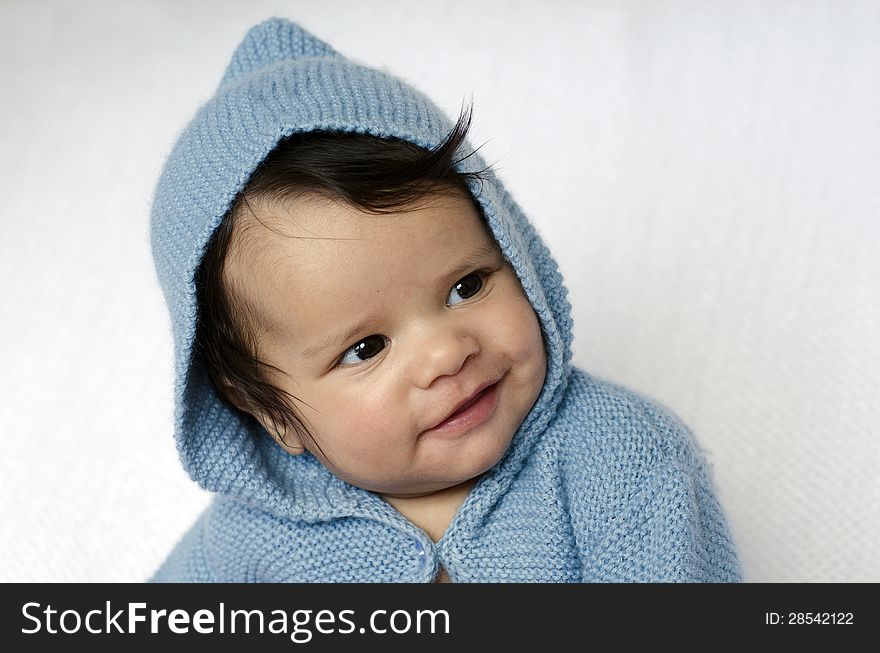 A newborn baby is wearing blue cardigan with hood smiles on a soft white background. Use the photo to represent life, parenting or childhood. A newborn baby is wearing blue cardigan with hood smiles on a soft white background. Use the photo to represent life, parenting or childhood.