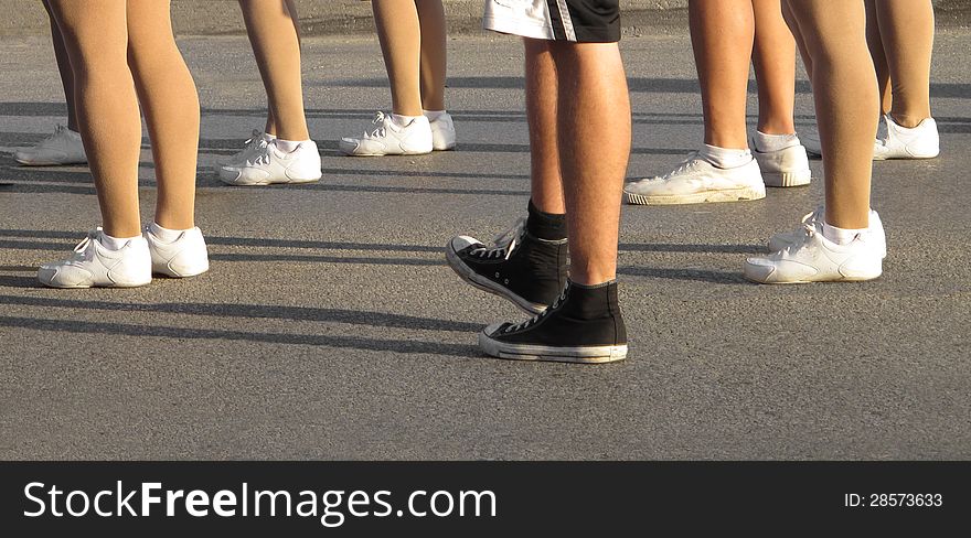 Lower bare legs of several people standing on a street, wearing white running shoes with one person wearing a black pair. Room at bottom for copy or text. Lower bare legs of several people standing on a street, wearing white running shoes with one person wearing a black pair. Room at bottom for copy or text.