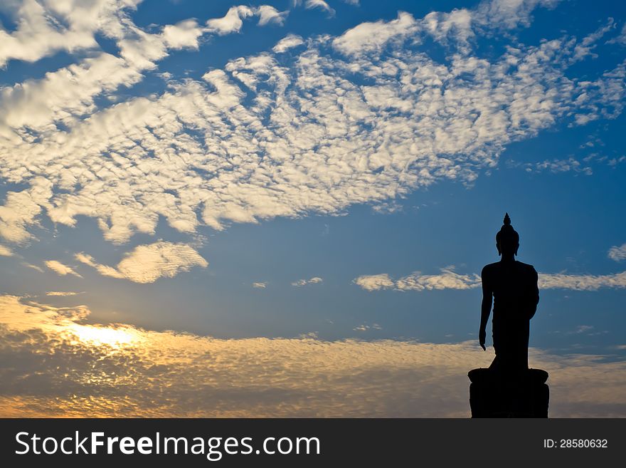 Silhouette of buddha statue with sunset in the cloudy day