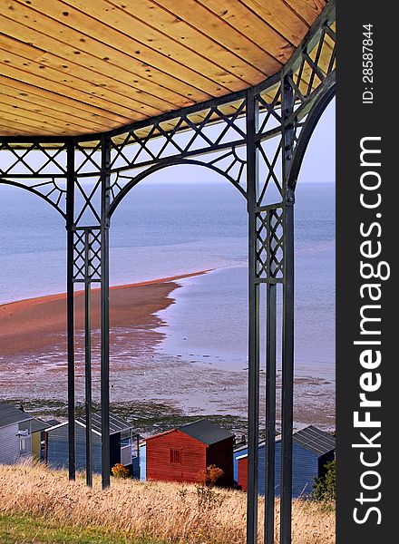 Photo of a bandstand structure overlooking beach huts at low tide on the coast of whitstable in kent. Photo of a bandstand structure overlooking beach huts at low tide on the coast of whitstable in kent.