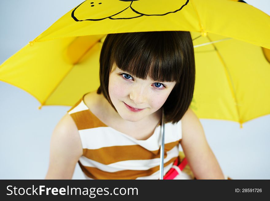 Colour portrait of a pretty young girl smiling under a fun yellow umbrella. Colour portrait of a pretty young girl smiling under a fun yellow umbrella.