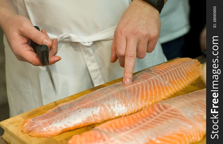 Cooks hands preparing fresh salmon fish. Image taken closeup with cooks hands testing the quality of a big piece of fresh salmon fish. Cooks hands preparing fresh salmon fish. Image taken closeup with cooks hands testing the quality of a big piece of fresh salmon fish.