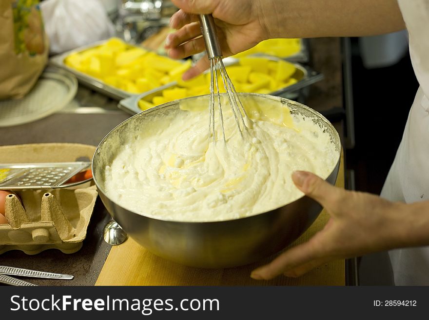 Baker is beating cheese creme for a cake with a swirl. Image taken closeup while beating the creme in a big bowl of steel.