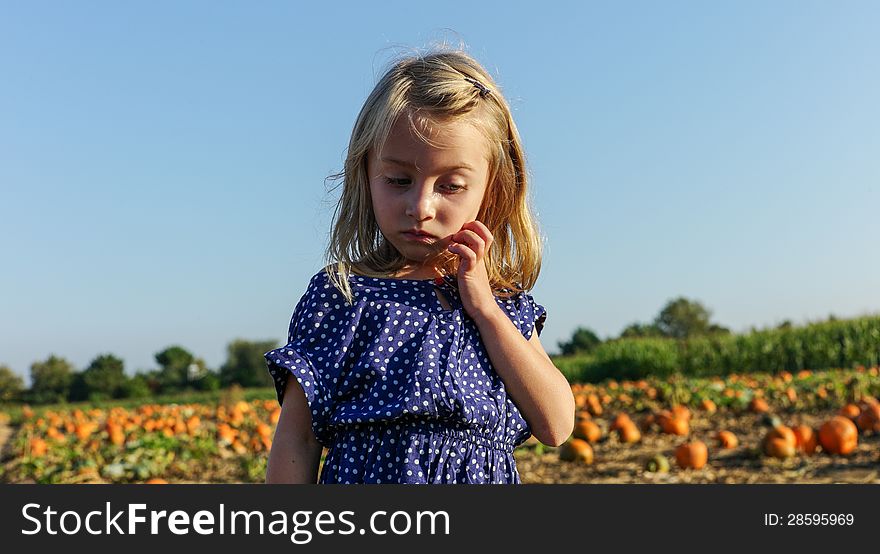 Little girl trying to decide which pumpkin to choose first - completely overwhelmed in a large pumpkin patch. Little girl trying to decide which pumpkin to choose first - completely overwhelmed in a large pumpkin patch