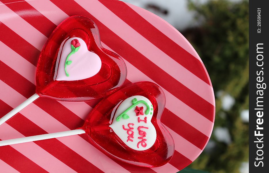 Pink and red striped plate with sugar heart lollipops, decorated with words and flowers to symbolize love on valentine's day. Pink and red striped plate with sugar heart lollipops, decorated with words and flowers to symbolize love on valentine's day.