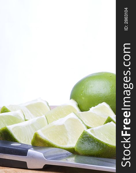 A selection of freshly cut limes with knife in foreground and whole lime in background. A selection of freshly cut limes with knife in foreground and whole lime in background