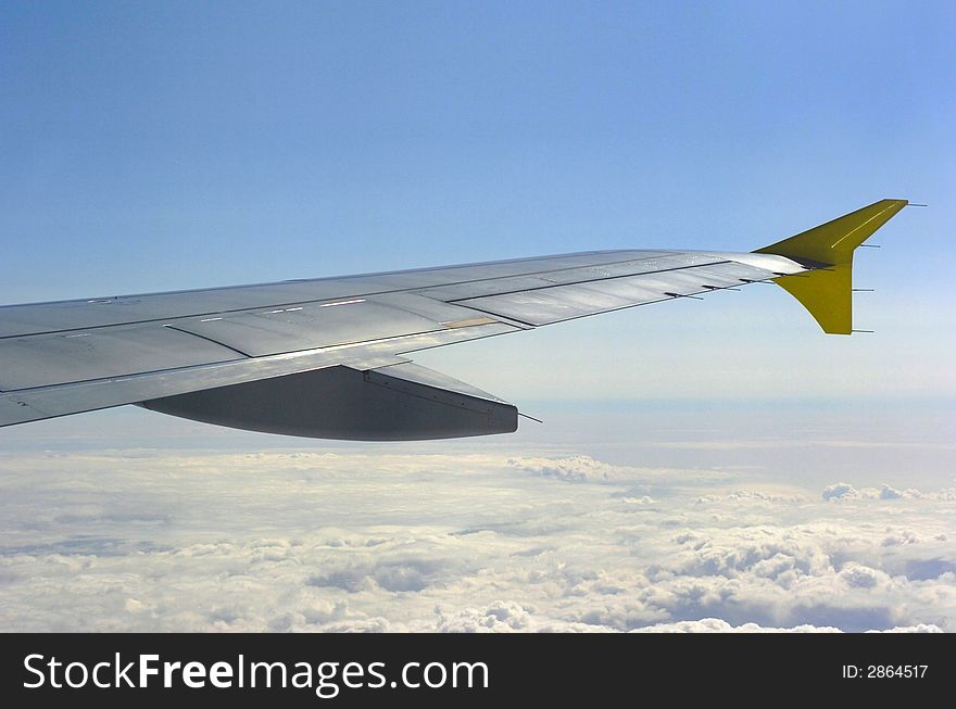 Aircraft winglet in the sun over the clouds up in blue sky