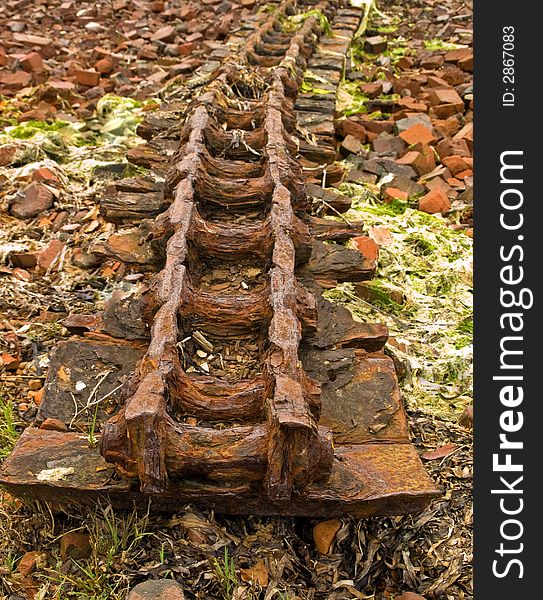 Old rusty bulldozer track among broken bricks