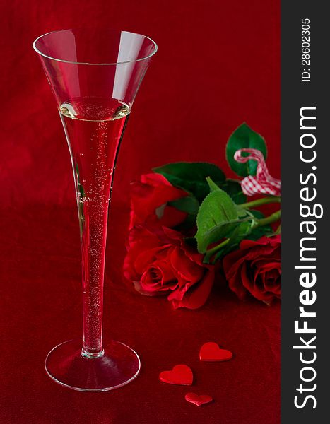 A glass of champagne and red roses for Valentine's Day on a red background. A glass of champagne and red roses for Valentine's Day on a red background