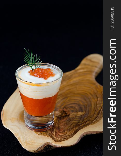 Appetizer of sweet pepper, cream and red caviar in a glasses on a wooden board on a black background