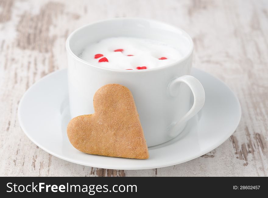 Cup of hot milk with foam, decorated with sugar hearts and heart-shaped cookies on the table