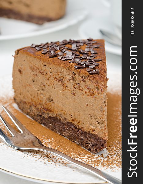 Piece of chocolate cheesecake sprinkled with cocoa and a fork on a white plate. Piece of chocolate cheesecake sprinkled with cocoa and a fork on a white plate