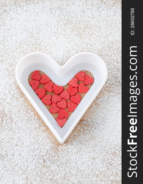 Sugar hearts in white baking dish on a board sprinkled with powdered sugar on a wooden board