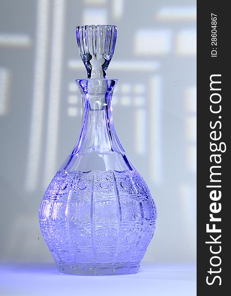 Decanter of cut glass lit with blue light in front of phantasy background, insinuating architecture. Decanter of cut glass lit with blue light in front of phantasy background, insinuating architecture