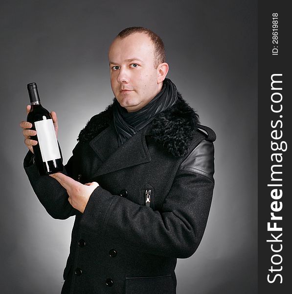 Handsome young man in winter coat with a bottle of wine on a gray background. Handsome young man in winter coat with a bottle of wine on a gray background