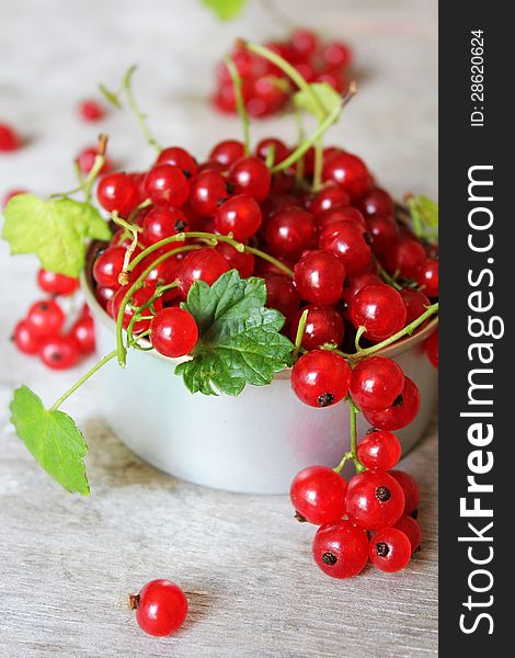 Red currant berries with green leaves in a cup on a wooden surface