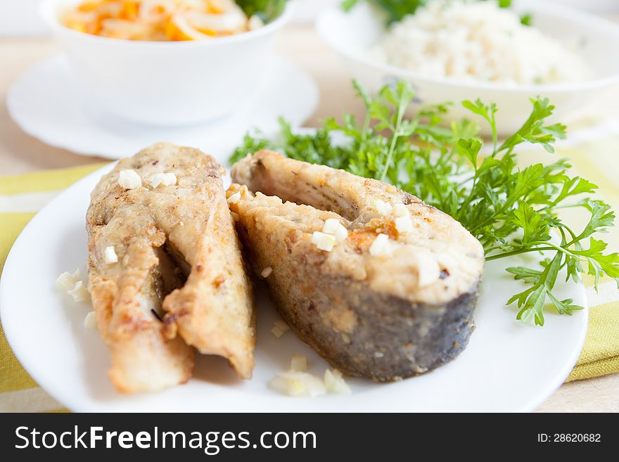 Fried fish slices on a plate with greens