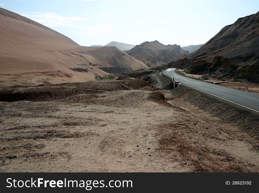 Road through a valley in a Taklamakan desert, Xinjiang, western China. The road follows the route of the ancient northern silk road. Road through a valley in a Taklamakan desert, Xinjiang, western China. The road follows the route of the ancient northern silk road