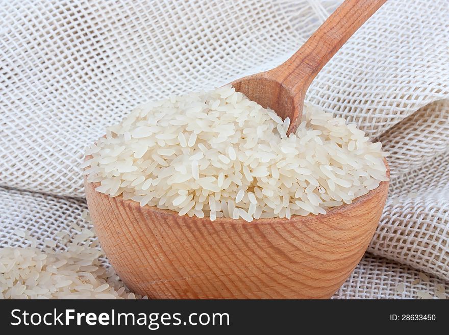 Raw white rice in wooden bowl and spoon on burlap, food ingredient photo