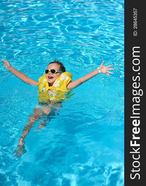 In the sunny day in the summer the boy in sun glasses and in a life jacket floats in pool. In the sunny day in the summer the boy in sun glasses and in a life jacket floats in pool