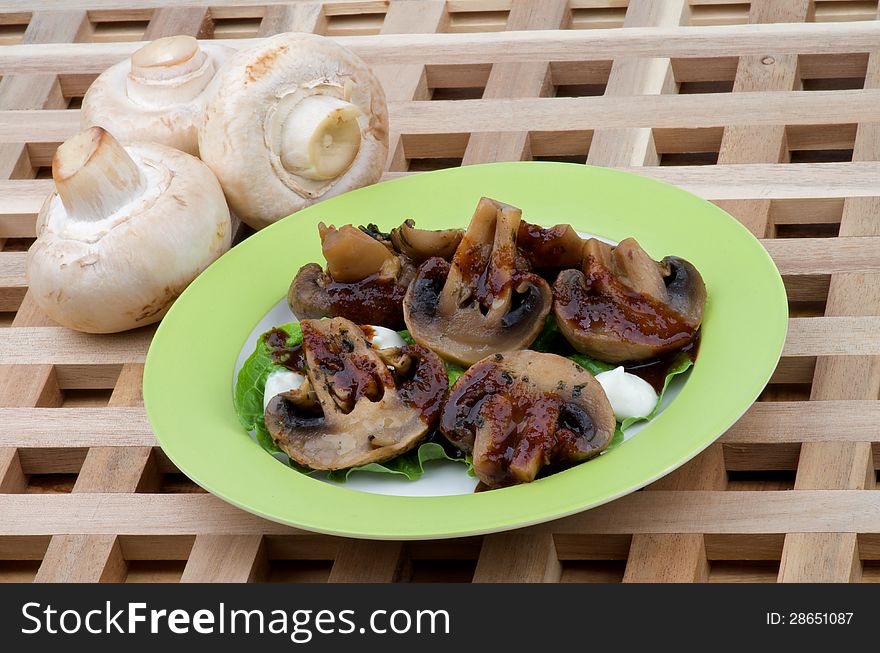 Perfect Grilled Mushrooms Champignons with Grill Sause, Lettuce and Sour Cream on Green Plate closeup on Wood background and Raw Mushrooms. Perfect Grilled Mushrooms Champignons with Grill Sause, Lettuce and Sour Cream on Green Plate closeup on Wood background and Raw Mushrooms