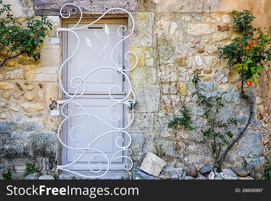 Provence white door in brick wall with metal bars, flowers on the wall. Provence white door in brick wall with metal bars, flowers on the wall