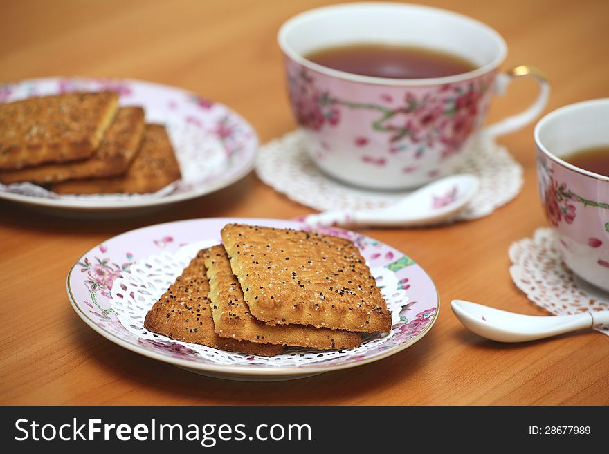Cookies served with tea in pink china cups with floral pattern on a wooden table. Cookies served with tea in pink china cups with floral pattern on a wooden table