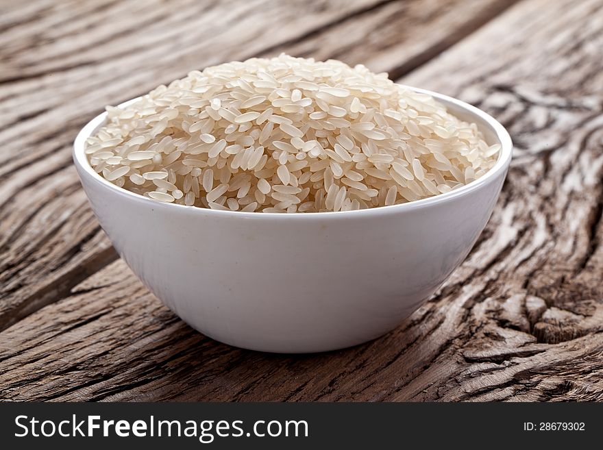 Uncooked rice in a bowl on a dark wooden table.