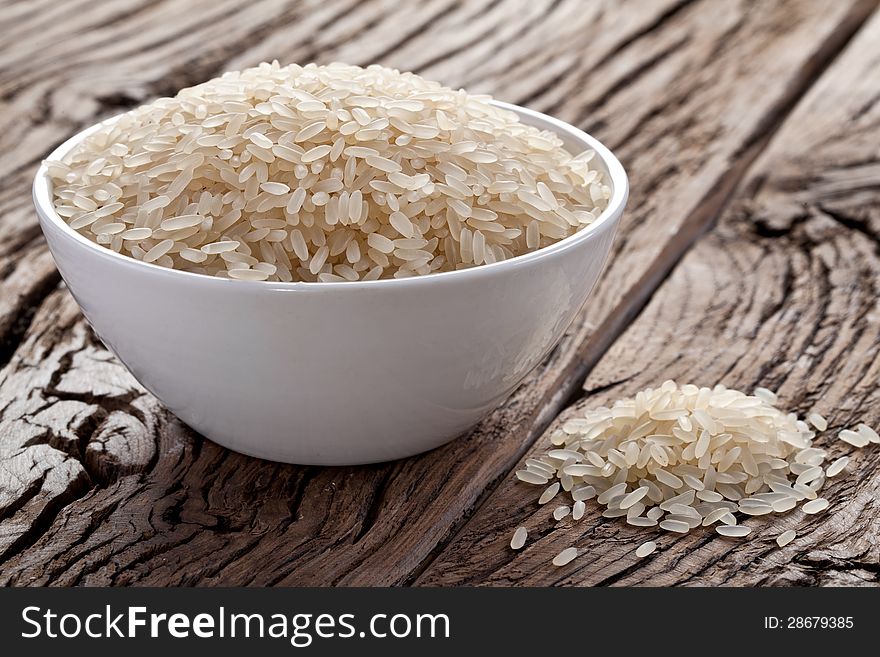 Uncooked rice in a bowl on a dark wooden table.