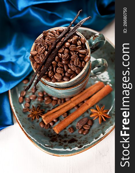 Coffee beans with cinnamon and vanilla in a blue cup on a vintage board