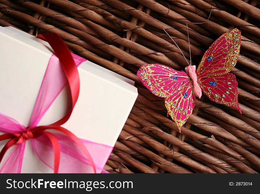 Gift box decorated with ribbons and a butterfly next to it on a woven wood surface. Gift box decorated with ribbons and a butterfly next to it on a woven wood surface