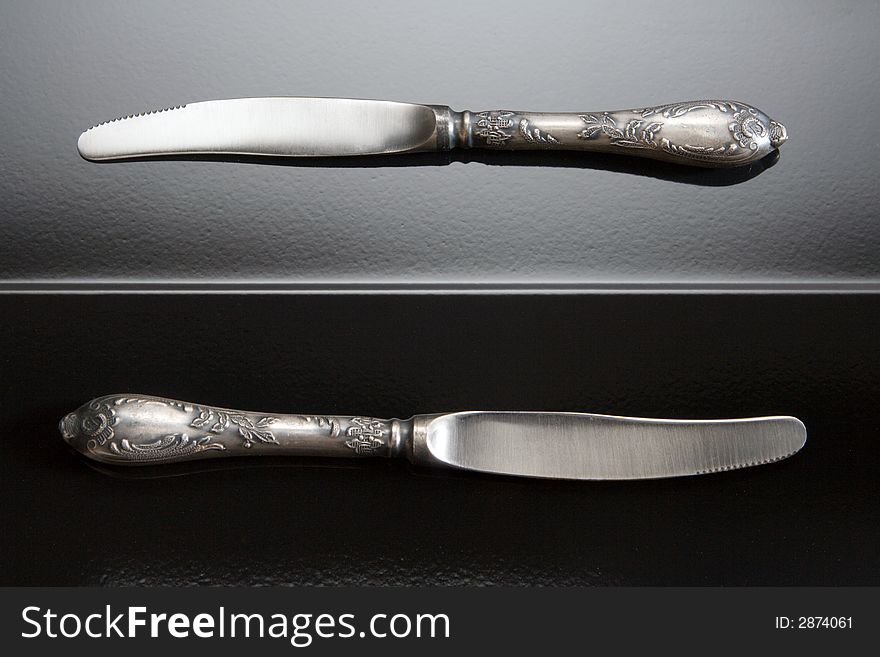 Two table knifes at black steel background.