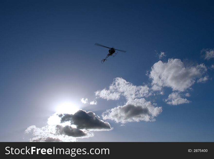 A silhouette of a helicopter with the sun hidden behind scattered clouds and a nice blue sky. A silhouette of a helicopter with the sun hidden behind scattered clouds and a nice blue sky.
