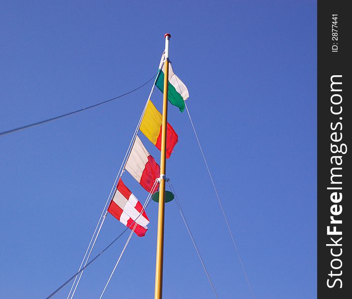 Four marine signal flags on wooden mast in blue sky. Four marine signal flags on wooden mast in blue sky