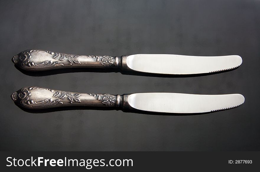 Two table knifes at black steel background.