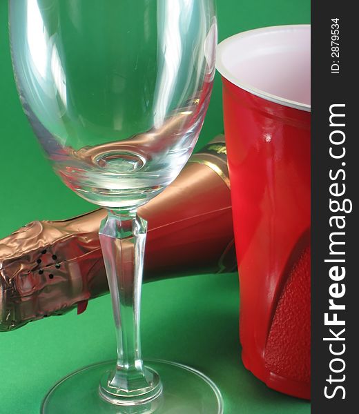 Champagne bottle and stemmed glass, red disposable cup, celebration against green background. Champagne bottle and stemmed glass, red disposable cup, celebration against green background