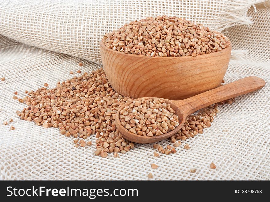 Raw buckwheat in wooden bowl and spoon on burlap, food ingredient photo