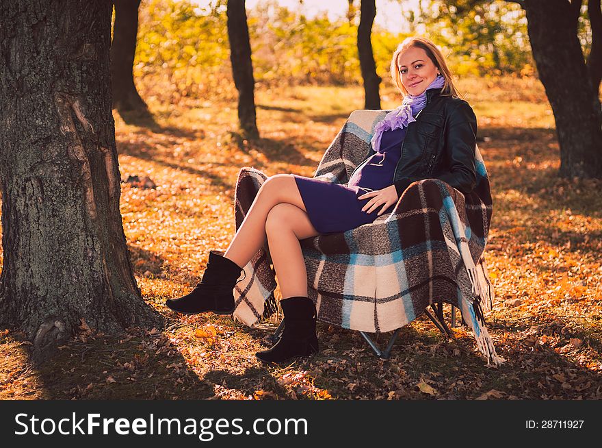 Young pregnant woman sitting on armchair in autumn forest. Young pregnant woman sitting on armchair in autumn forest