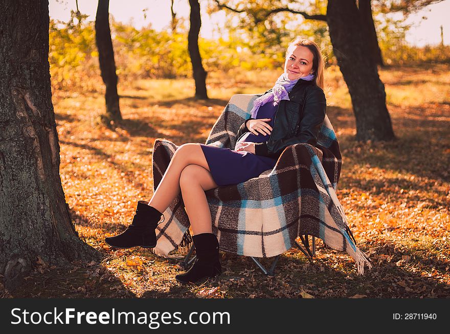 Young pregnant woman sitting on armchair in autumn forest. Young pregnant woman sitting on armchair in autumn forest