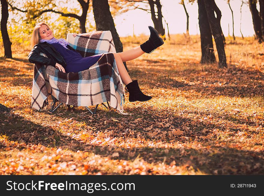 Young pregnant woman sitting on armchair in autumn forest. Young pregnant woman sitting on armchair in autumn forest