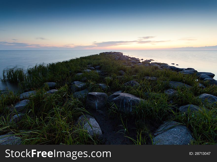 Summer morning landscape on lake with a rocky shore and grass