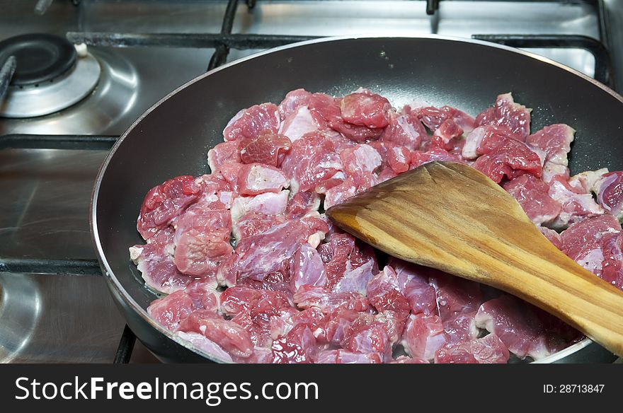 Sliced â€‹â€‹meat begins is fried in a pan and wooden spoon