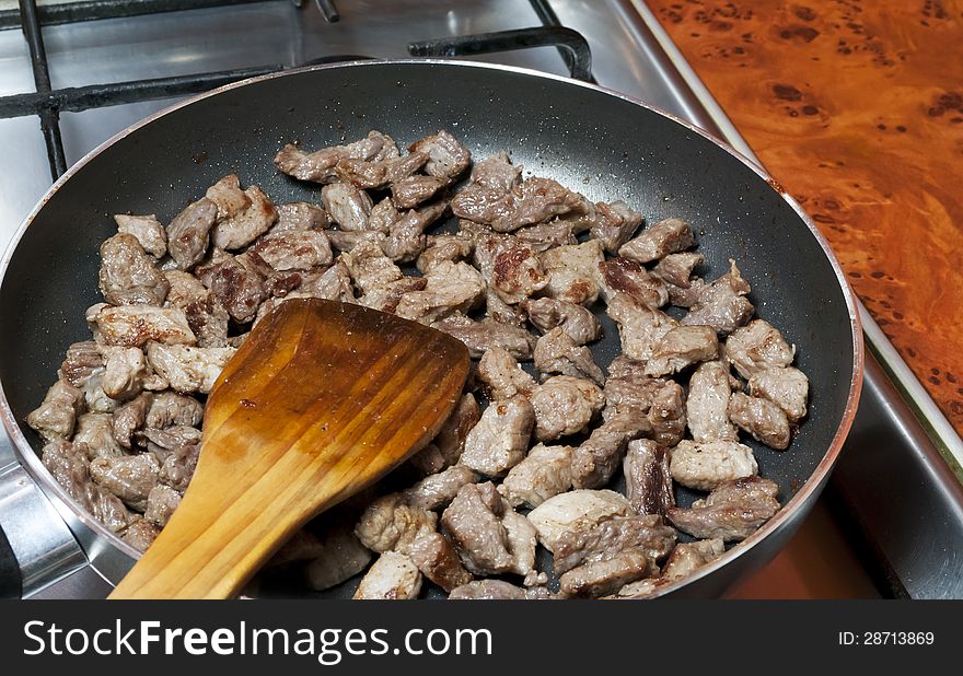 Sliced meat fried in a pan and wooden spoon