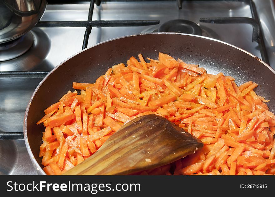 Sliced carrots fried in a pan and wooden spoon