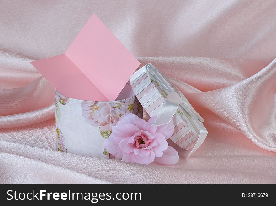 Gift box with a card and a pink flower on pink silk. Gift box with a card and a pink flower on pink silk