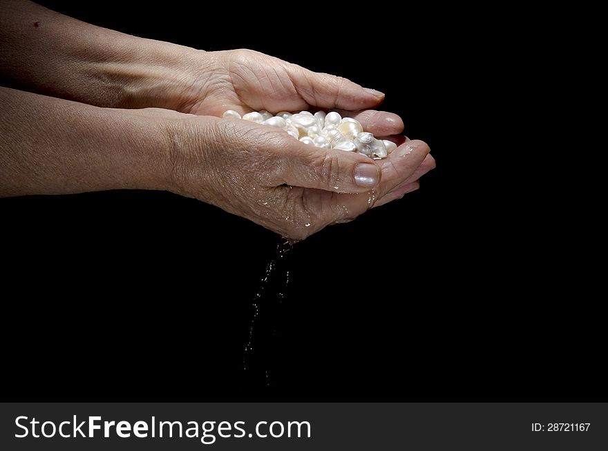 Pearls in female palms of old woman isolated on black background. Pearls in female palms of old woman isolated on black background