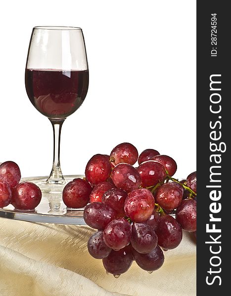 A bunch of red grapes on a glass plate and a glass of wine. A bunch of red grapes on a glass plate and a glass of wine