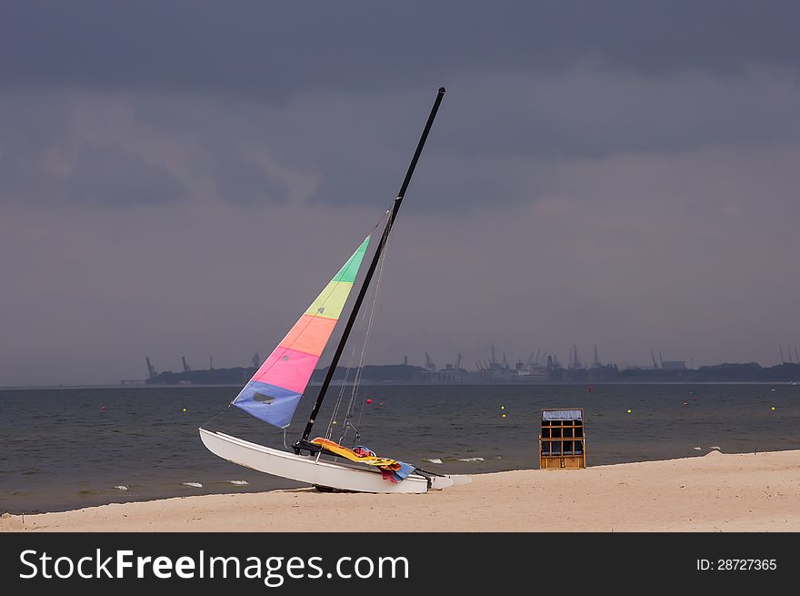 Colorful sailboat on the beach in Sopot, Poland, with the stormy clouds and Gdansk Shipyard in the background.